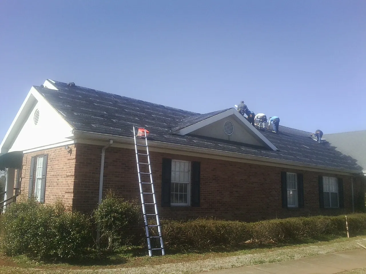 Crew tearing shingles off a brick ranch roof with a ladder set — Metal Roof Repair work by our crew in Delphi