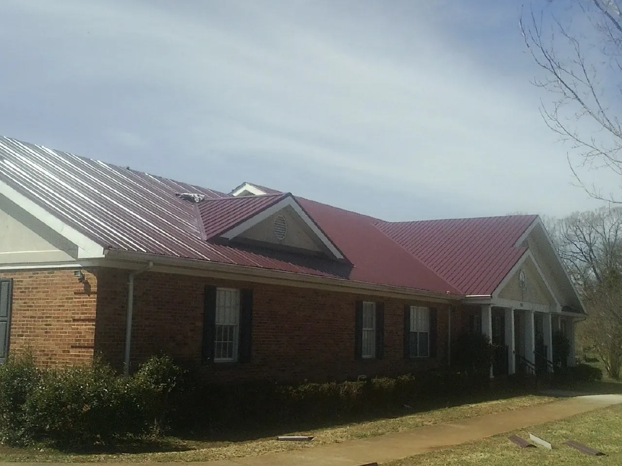 Red metal roof with gabled entries on a long brick building, from a Hail Damage Roof Repair job in Delphi