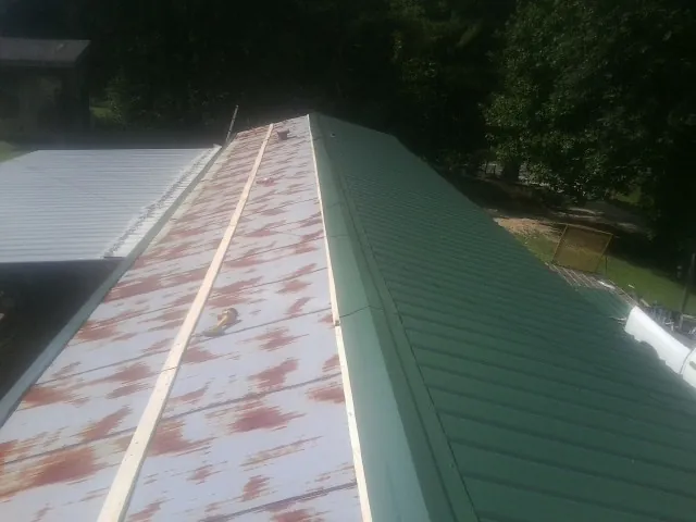 Old rusted panels beside newly installed green metal roofing — Wind Damage Roof Repair by Roofing Brothers in Delphi