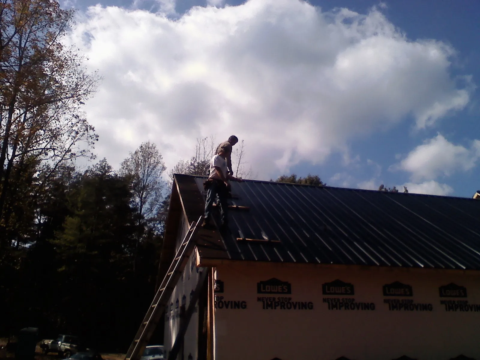 Roofer fastening dark metal panels high against a cloudy sky, from a Roof Inspection job in Delphi