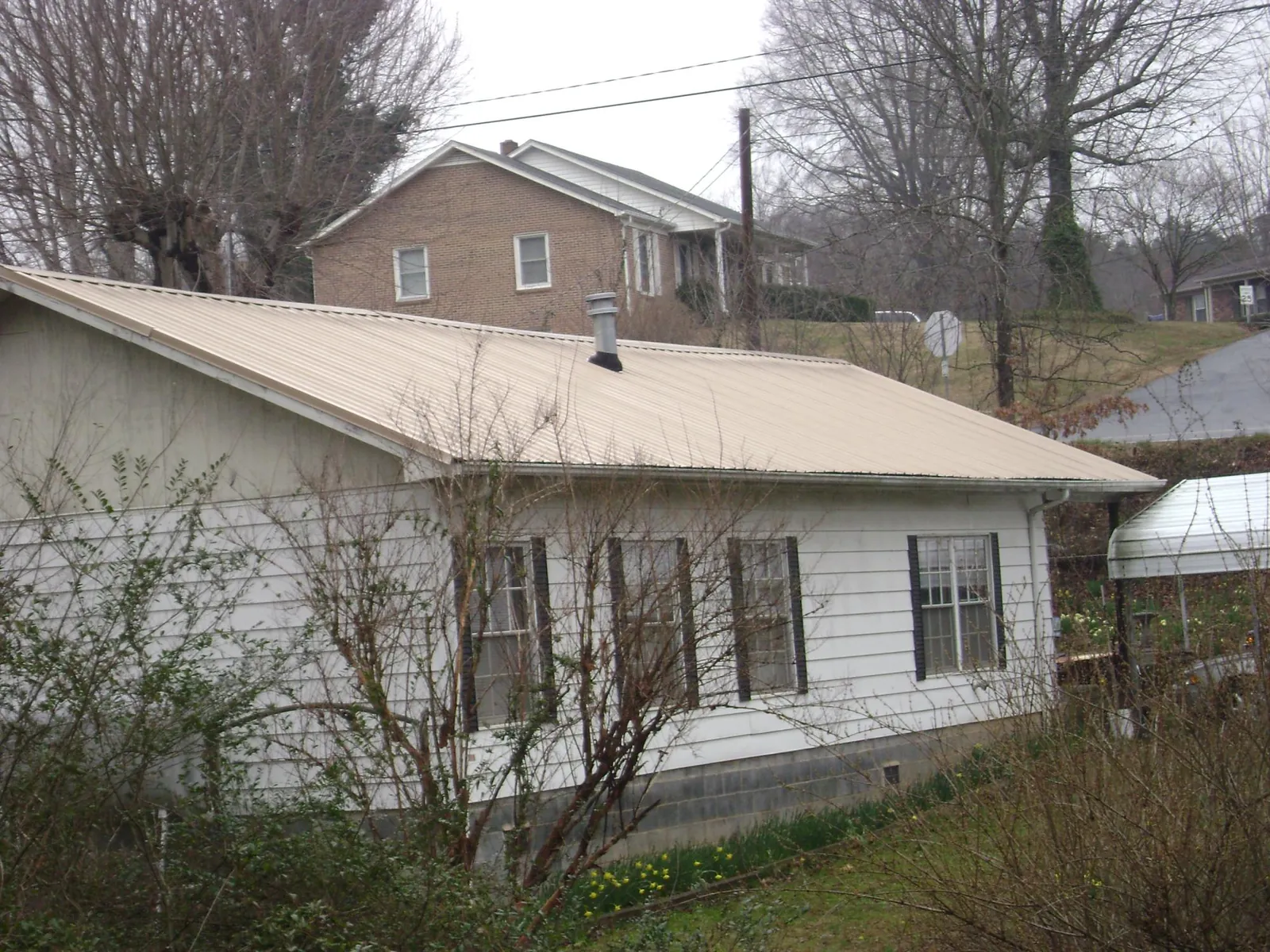Tan metal roof on a white sided house set into a hillside — Commercial Roofing by Roofing Brothers in Delphi